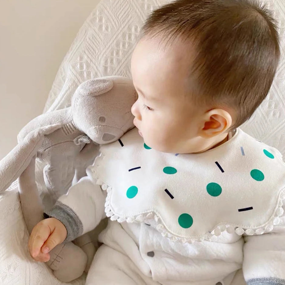 Baby wearing a bib with green polka dots, holding a gray plush toy.